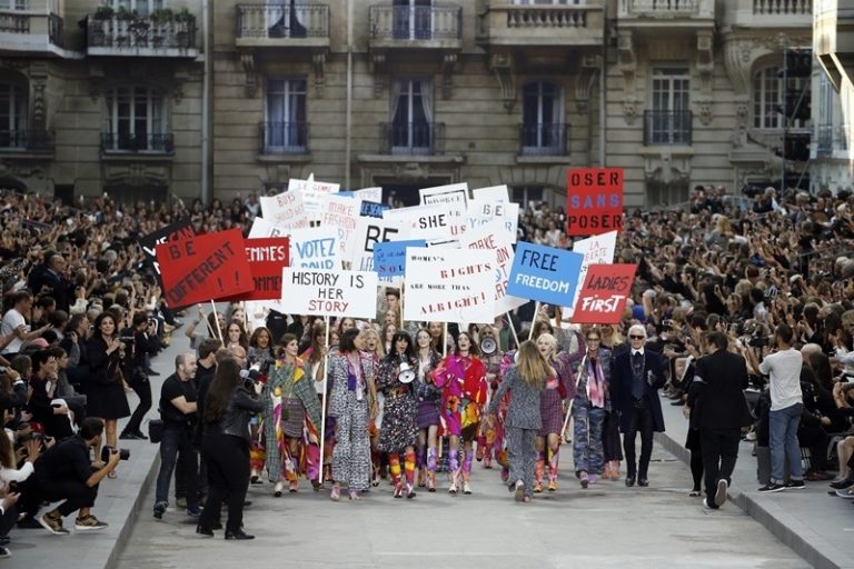 Models fake a demonstation as they present creations for Chanel next to German fashion designer Karl Lagerfeld (R) during the 2015 Spring/Summer ready-to-wear collection fashion show, on September 30, 2014 at the Grand Palais in Paris. AFP PHOTO / PATRICK KOVARIK        (Photo credit should read PATRICK KOVARIK/AFP/Getty Images)